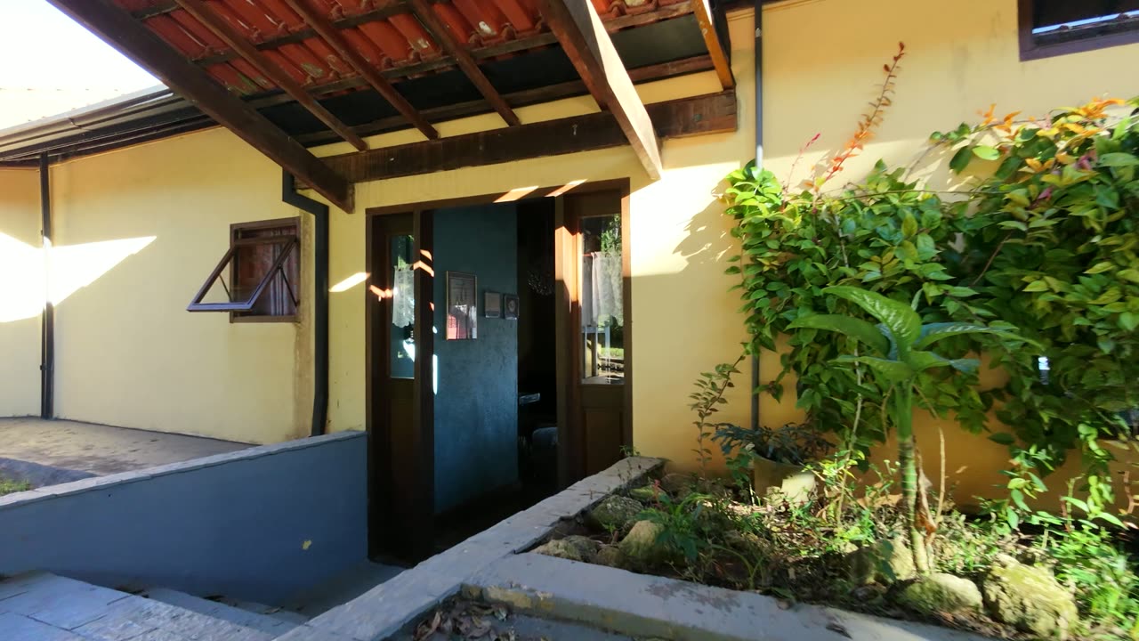 Sala comprida da casa principal, com mesa grande e as portas abertas para o vale.